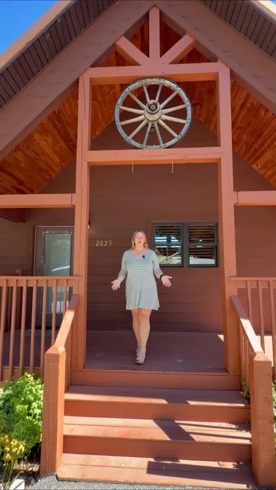 Guest on red wooden steps of a cabin with a wagon-wheel gable