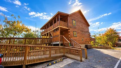 Large log cabin with wraparound deck among autumn trees